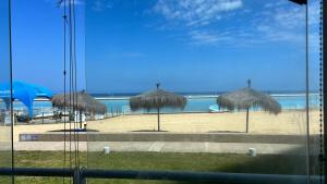 una playa con algunas sombrillas de paja y el océano en Departamento San Alfonso del Mar, primer piso, en Algarrobo