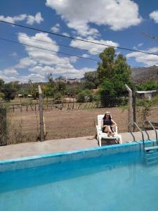 una mujer sentada en una silla junto a una piscina en Complejo de Cabañas Las Mellizas en San Agustín de Valle Fértil