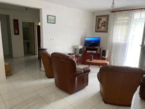 a living room with leather chairs and a television at Villa léïna, vacances en famille écotourisme in Le Robert
