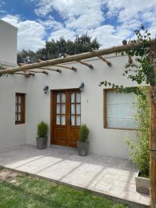 Casa blanca con puerta de madera y algunas plantas en EL TOPON cabañas en Albardón