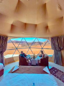 2 personas sentadas en sillas en una habitación con una gran ventana en Wadi Rum Relaxation Camp en Wadi Rum