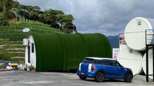 une petite voiture bleue garée à côté d'un bâtiment vert dans l'établissement Cameron Highlands Blueberry Earth House, à Cameron Highlands