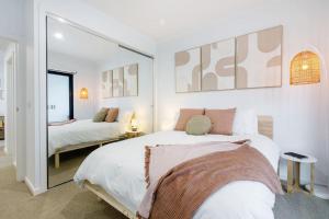 a white bedroom with two beds and a mirror at 'Laidback Lygon' A Two-storey Inner-city Oasis in Melbourne