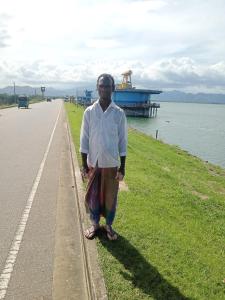 a man standing next to a road next to the water at River Edge Udawalawe in Udawalawe