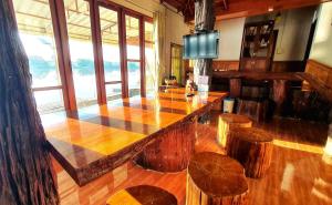 - un grand bar en bois avec tabourets dans une pièce avec fenêtres dans l'établissement Ruen Thai Ban Rim Nam, à Kamphaeng Phet