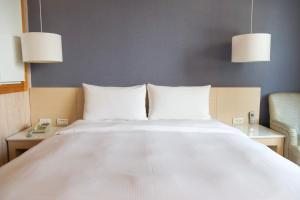 1 cama con sábanas blancas, 2 mesas y 2 lámparas en Kindness Hotel - Kaohsiung Guang Rong Pier, en Kaohsiung