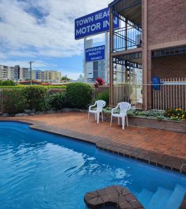 two chairs and a swimming pool in front of a building at Town Beach Motor Inn Port Macquarie in Port Macquarie