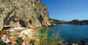 a beach with people in the water next to a mountain at UNA HOTELS Capotaormina in Taormina