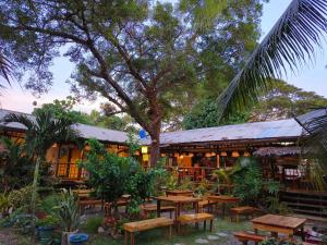 a restaurant with wooden tables and benches and a tree at Lokal Hut Bed and Breakfast in Puerto Princesa City