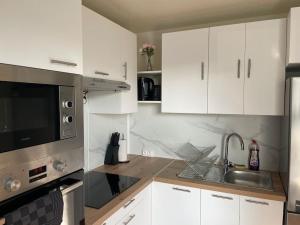 La cuisine est équipée de placards blancs, d'un évier et d'un four micro-ondes. dans l'établissement Appartement Cosy proche Paris, au Bourget
