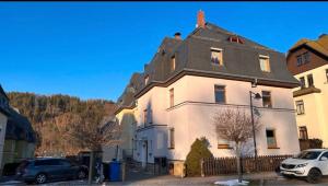 a white house with a black roof and cars parked in front at Stilvolles City-Apartment I WLAN l Küche I Zentral I 8P in Schwarzenberg