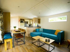 sala de estar con sofá azul y cocina en Recreatiepark Duinhoeve 13, en Udenhout