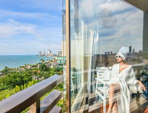 a woman sitting on a balcony with a view of the ocean at The Bayview Hotel Pattaya in Pattaya