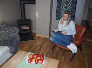 a woman sitting in a chair reading a book with a plate of apples at Cabin with great view close to town and ski area in Lillehammer +17 photos