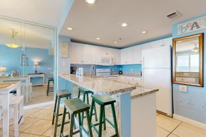 デスティンにあるSterling Shores 510 Destin (Condo)の青い壁と白いキャビネット、バースツール付きのキッチン