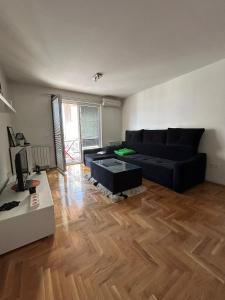 uma sala de estar com um sofá preto e um piso de madeira em Apartman SARA em Sarajevo