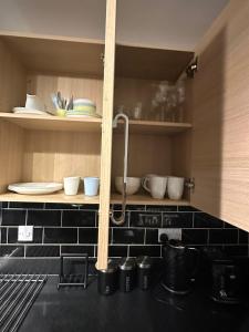 una cocina con encimeras de azulejos negros y estanterías con platos en Lakeside apartment with FREE parking / M25 en Purfleet