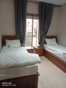 two beds in a room with a window at Appartement Prestigia Marrakech in Marrakech