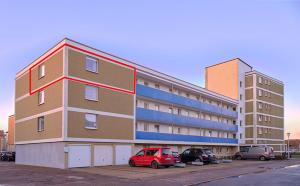 a large building with a red car parked in a parking lot at Komfort Appartement Sylt - direkt am Strand - in Westerland (Sylt)
