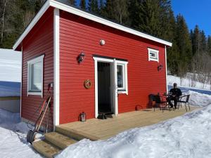 un hombre sentado en el porche de una casa roja en la nieve en Solbergs, fint attefallshus i Vik, Åre en Åre