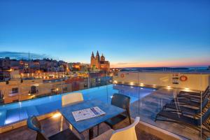 a table on a balcony with a view of a city at Pergola Hotel & Spa in Mellieħa