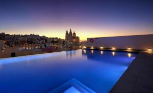 a rooftop pool with a view of a city at night at Pergola Hotel & Spa in Mellieħa