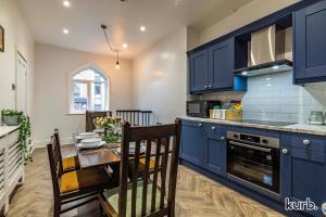 a kitchen with blue cabinets and a table with chairs at The Church House - 3 Bedroom House + Free Parking in Nottingham