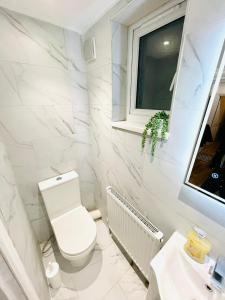 a white bathroom with a toilet and a window at Ravensbury Home in Mitcham