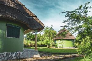 a green building with a thatched roof next to a house at Elephant View Lodge in Kasenyi
