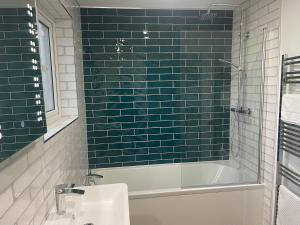 a bathroom with green subway tiles and a tub and a sink at Furzy House in Pembrokeshire