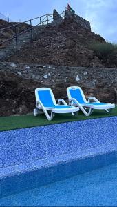 two blue and white lounge chairs next to a swimming pool at Alhara Lodge استراحة الحارة 