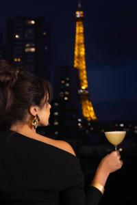 une femme tenant un verre de vin devant la tour de l'eiffel dans l'établissement Quinzerie hôtel, à Paris