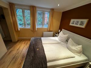 a bedroom with a bed with white sheets and two windows at Lucia's ElbHotelchen in Lauenburg