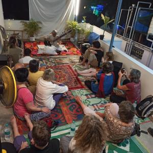 een groep mensen die op de vloer zitten te kijken naar een gitarist bij Bethesda Inn in Cochin