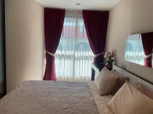 a bedroom with a bed and a window with red curtains at The Chezz by Apple & Frank in Pattaya Central