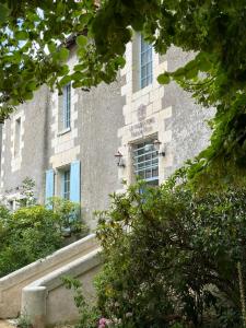 Le Presbytère • Maison Flore في Chédigny: مبنى نوافذه زرقاء وشجيرات أمامه