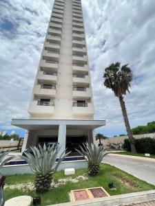 una torre blanca alta con una palmera frente a un edificio en Flat Particular - próx Assembleia Leg MT, en Cuiabá