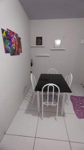 uma sala de jantar com uma mesa preta e cadeiras brancas em Stúdio Cozy em Palmas