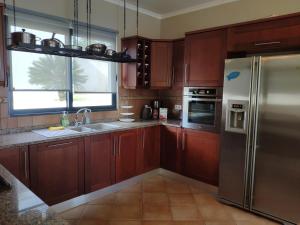 a kitchen with wooden cabinets and a stainless steel refrigerator at 17 ° West, Lux. Inf. Pool villa, 5 minutes to the sandy beach, WiFi in Estreito da Calheta