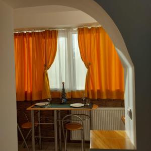 una mesa y sillas en una habitación con cortinas naranjas en Dayana Home en Râmnicu Vâlcea