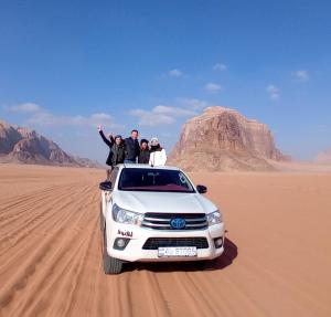 a group of people standing on top of a white car in the desert at Shakria Bedouin Life Camp in Wadi Rum