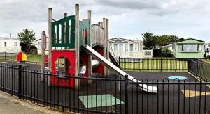a small playground with a slide in front of a fence at Caravan 521 shuker Barmouth in Talybont
