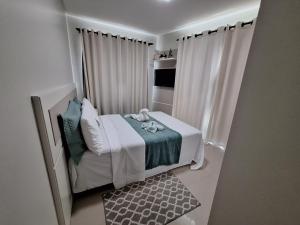 un pequeño dormitorio blanco con cama y cortinas en Apartamento praia Bombas com 2 quartos cobertura, en Bombinhas
