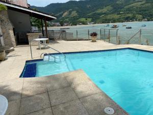 a large blue swimming pool next to a body of water at Angra Pier600 Casa beira mar in Angra dos Reis