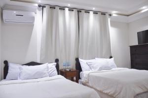 2 camas en un dormitorio con paredes y cortinas blancas en Hotel Villa Antigua en San Salvador