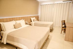 a hotel room with two beds and a desk at Confort Fronteira Hotel in Santana do Livramento