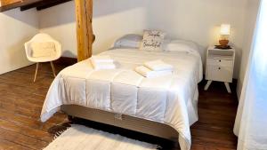 1 dormitorio con 1 cama con sábanas blancas y silla en Alma Andina en El Calafate