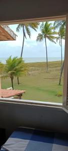 a window with a view of a beach with palm trees at Chalé Barra Sirinhaém in Sirinhaém