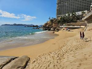 uma praia de areia com um edifício e o oceano em departamento con vista al mar em Acapulco