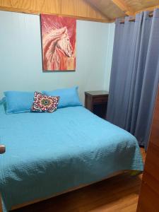 a bedroom with a blue bed with a painting of a horse at Cabañas Antumahuida Antuco in Antuco